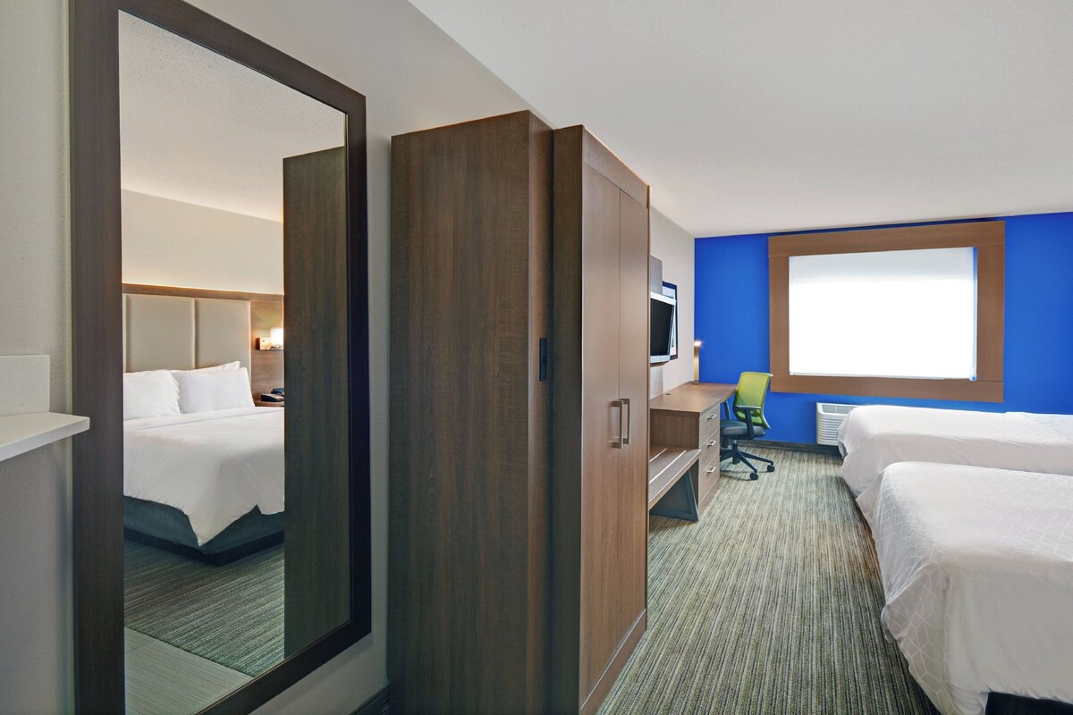 A hotel room with a large mirror, a wardrobe, a desk, and two beds.