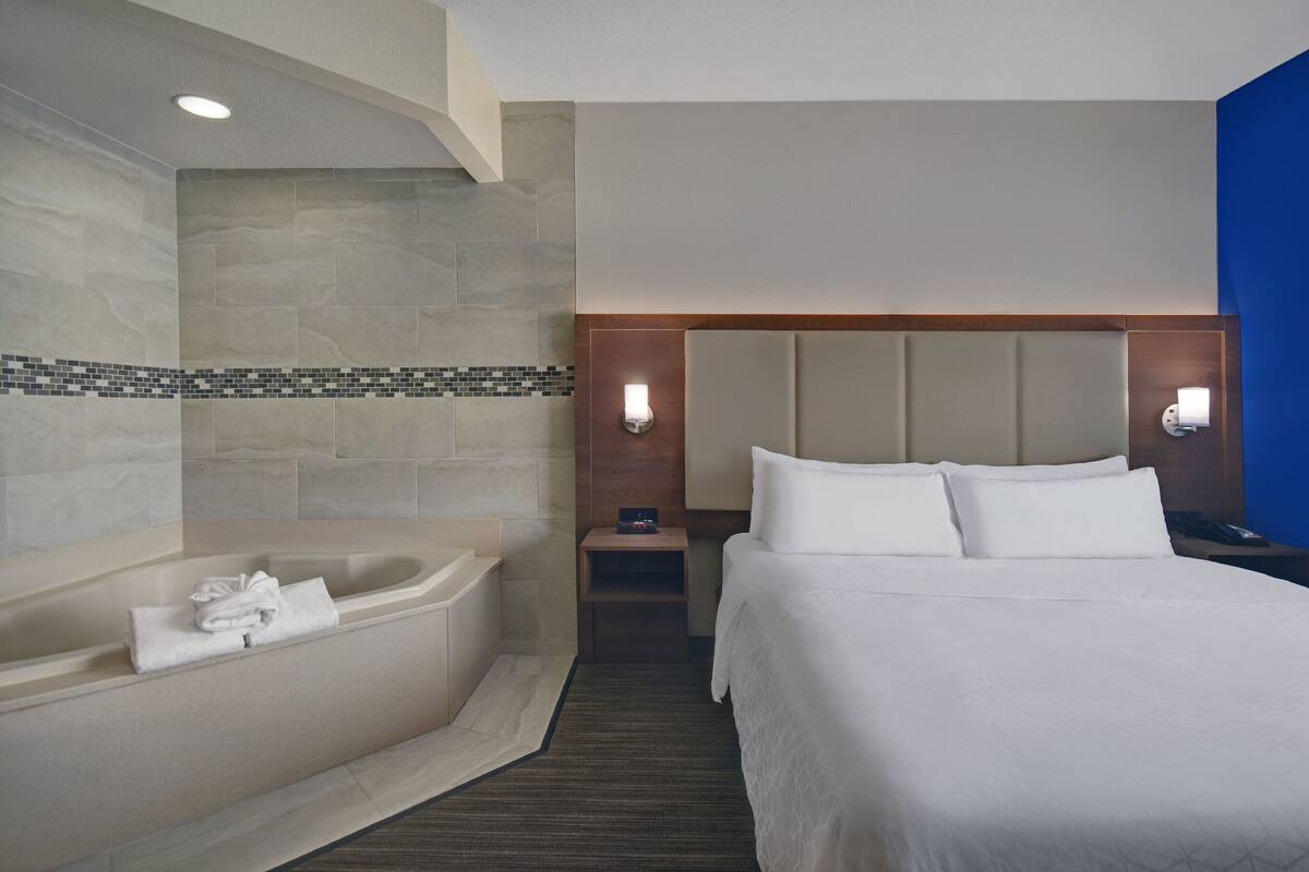 A hotel room with a large bed, a bathtub, and a nightstand with a lamp.