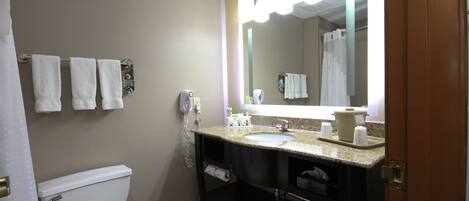 A bathroom with a toilet, sink, and mirror. There are towels hanging on the wall and a shower curtain.