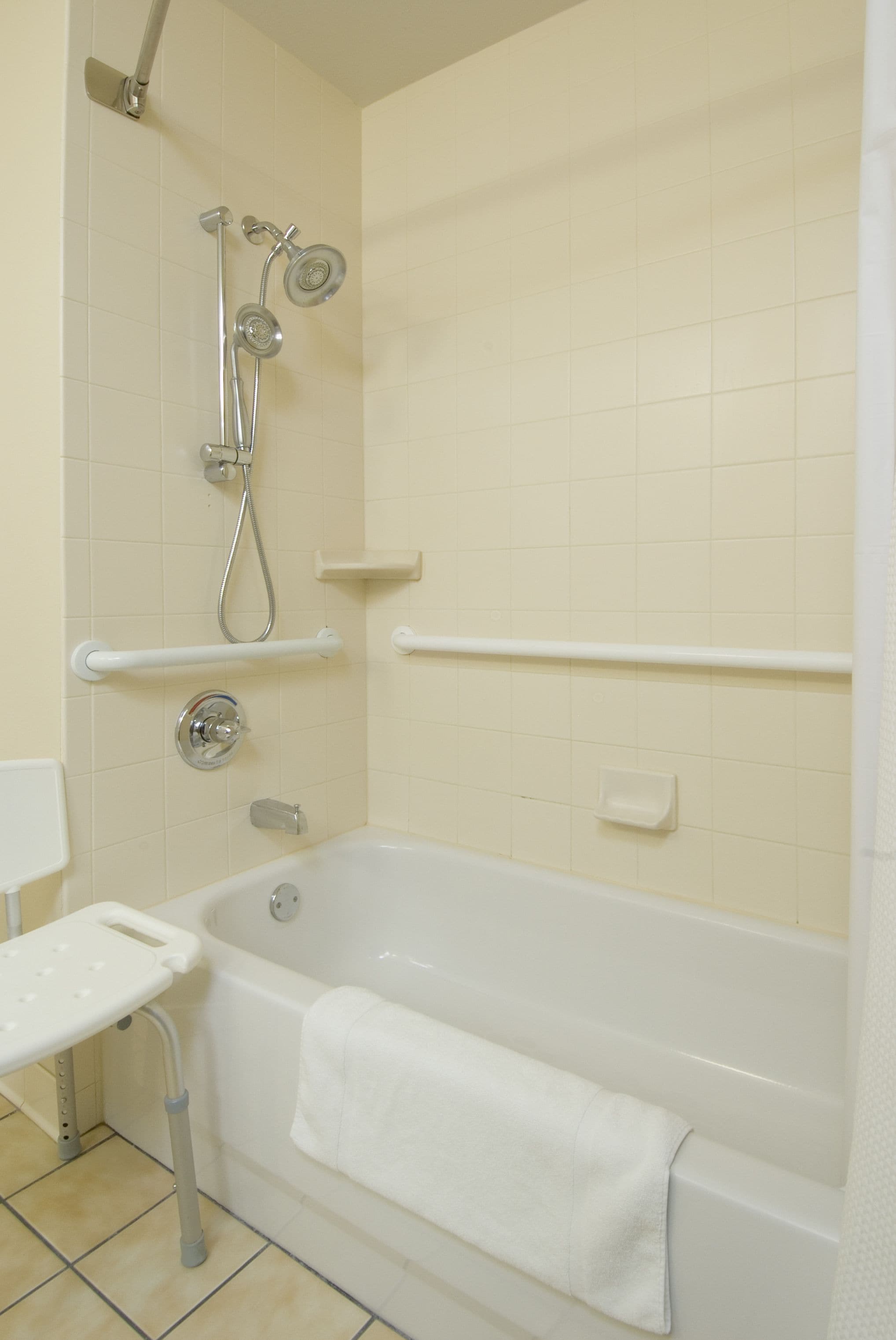 Un baño con bañera, ducha con cabezal de ducha manual, una toalla blanca y un estante blanco.