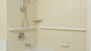 Un baño con bañera, ducha con cabezal de ducha manual, una toalla blanca y un estante blanco.