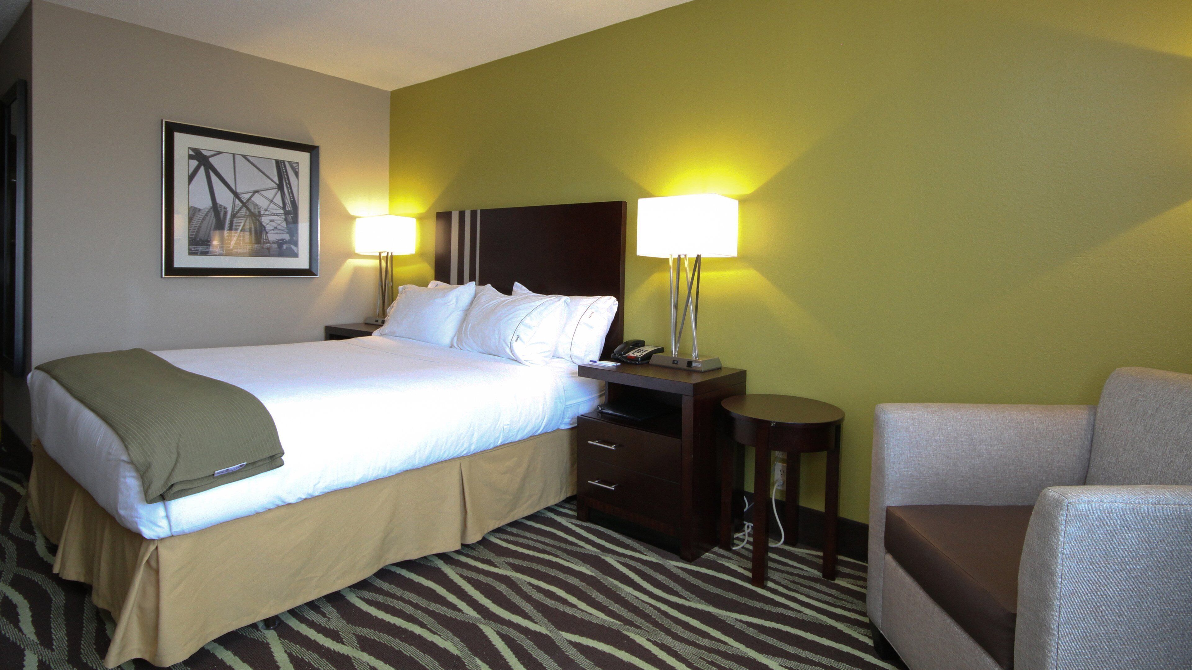 A hotel room with a bed, bedside tables, a chair, and a lamp.