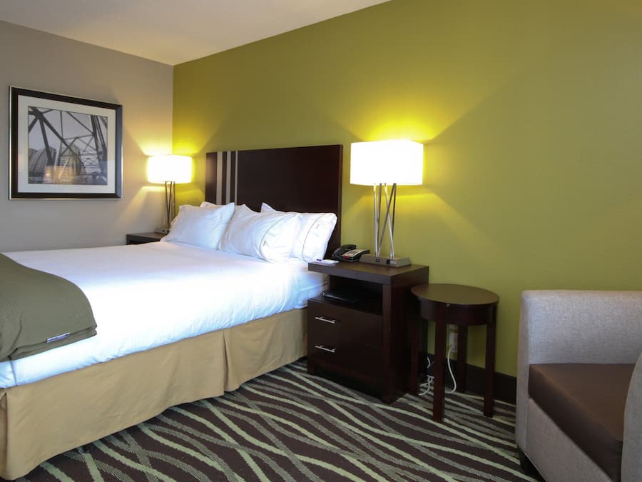 A hotel room with a bed, bedside tables, a chair, and a lamp.