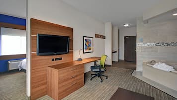Une chambre d’hôtel avec un bureau en bois, un téléviseur à écran plat, un tableau encadré, une chaise et une salle de bain équipée d’un porte-serviettes.