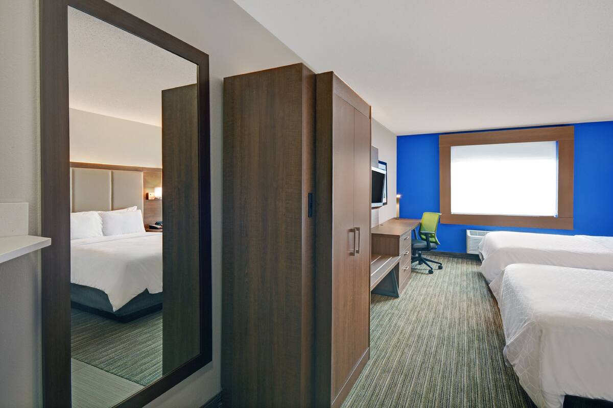 A hotel room with a large mirror, a wardrobe, a desk, and two beds.