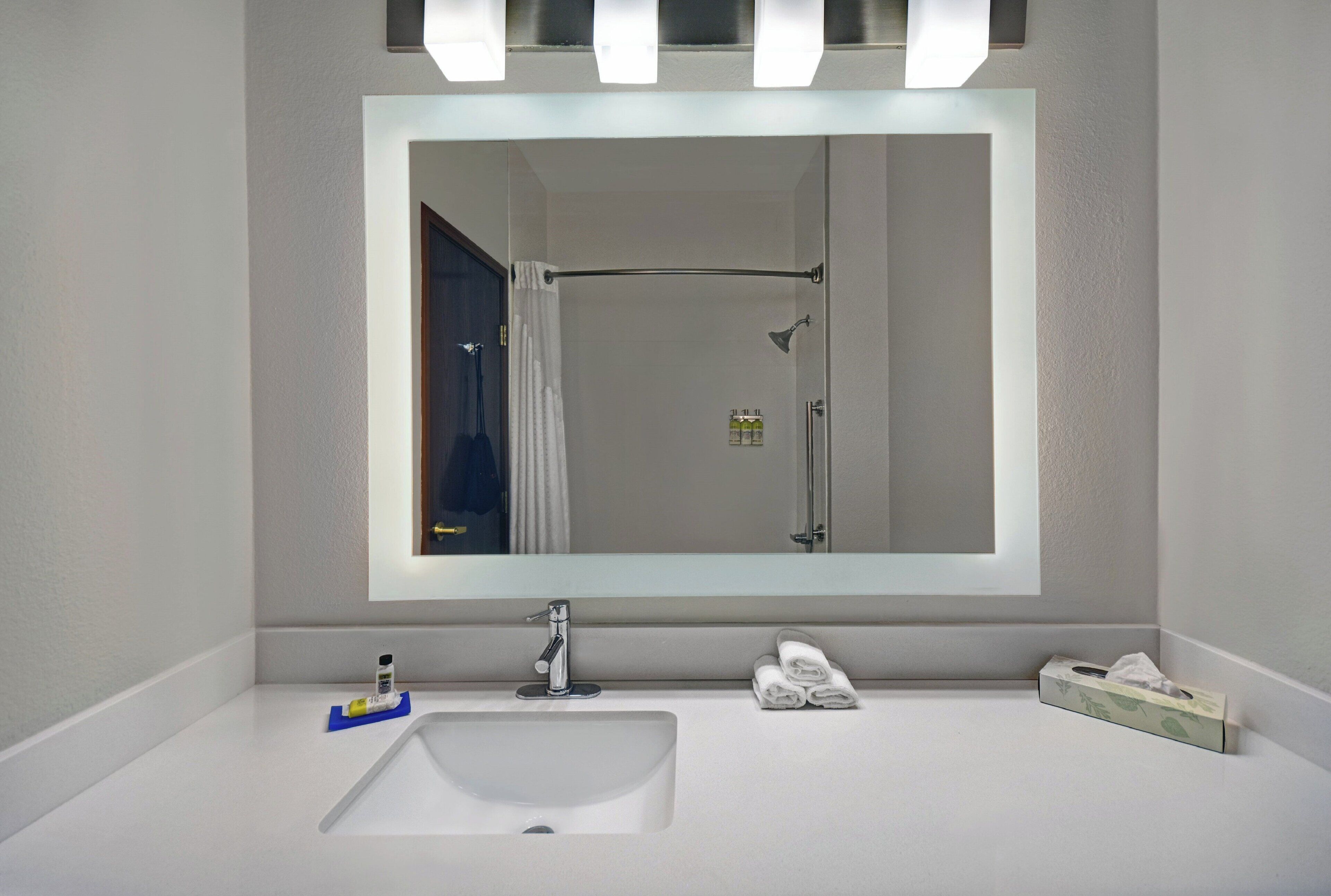 A bathroom with a large mirror, a sink, a shower, and a towel rack.