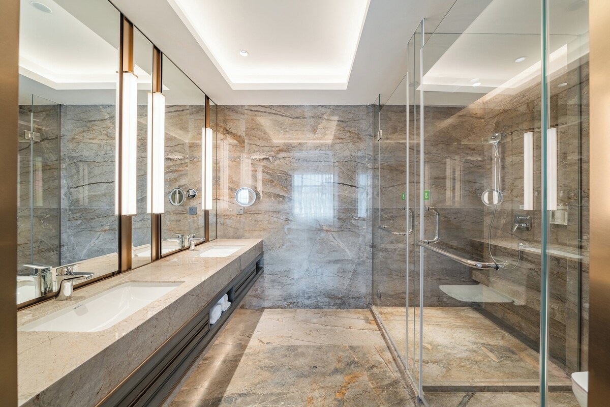 A modern bathroom with a glass-enclosed shower, marble walls, and a large mirror.
