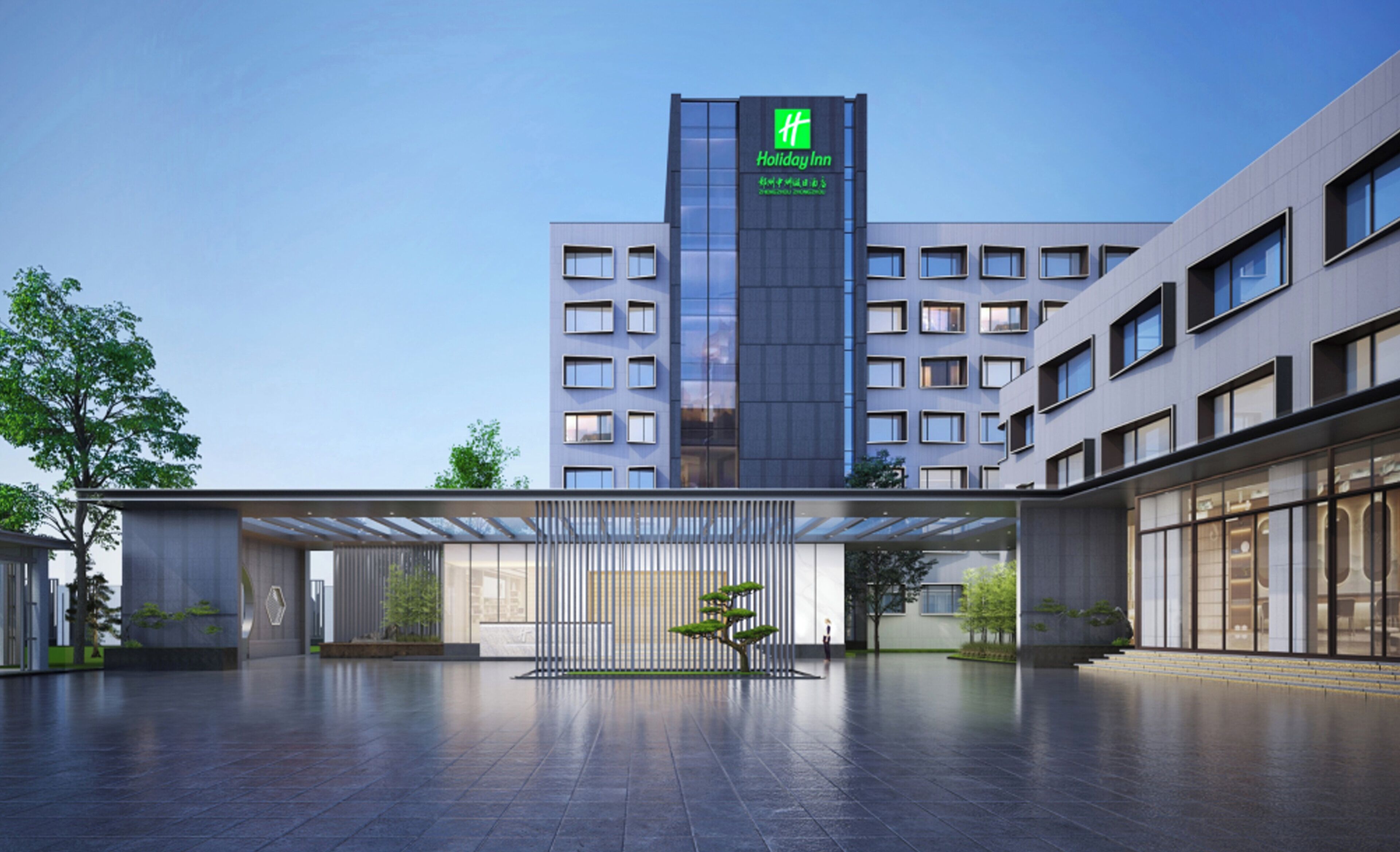Un hotel Holiday Inn con diseño moderno, destacando una torre con el logotipo del hotel, un área de entrada amplia con galería techada y un patio bien cuidado.