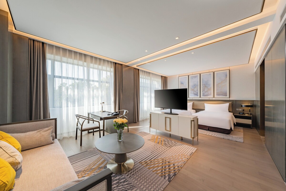A modern hotel room with a bed, a desk, a TV, and a sofa.