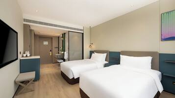 A hotel room with two beds, a desk, a TV, and a bathroom visible through an open door.