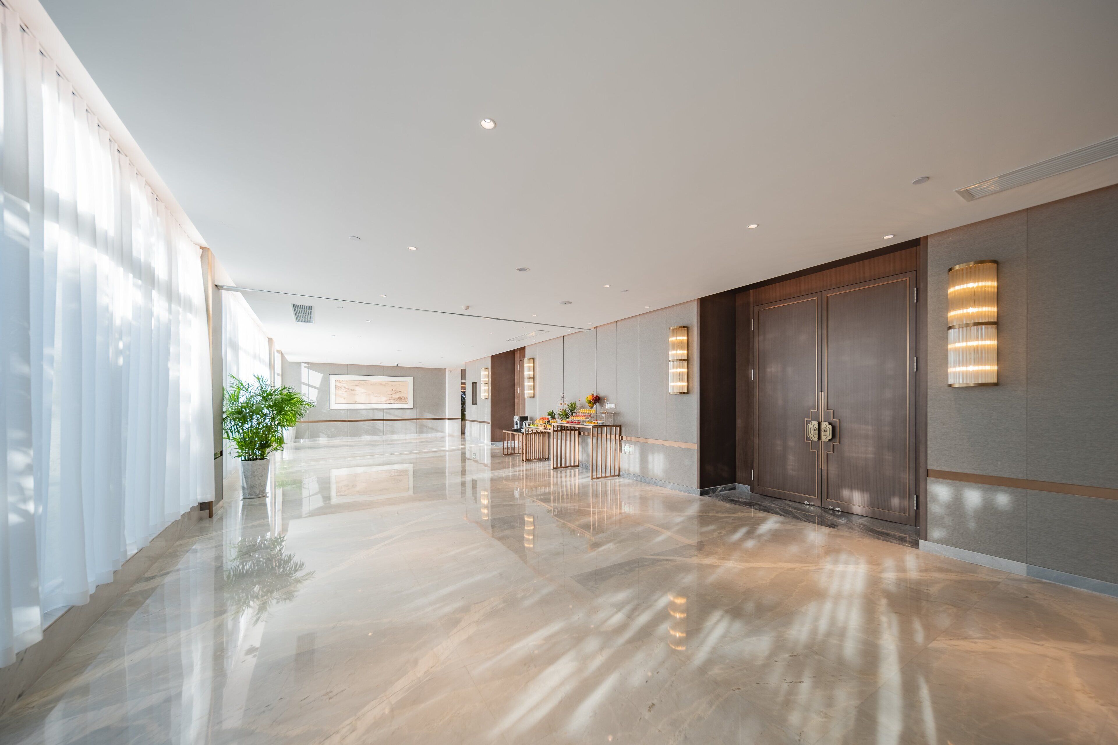 A spacious, modern hotel lobby with a polished floor, large doors, and a reception desk.