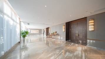 A spacious, modern hotel lobby with a polished floor, large doors, and a reception desk.