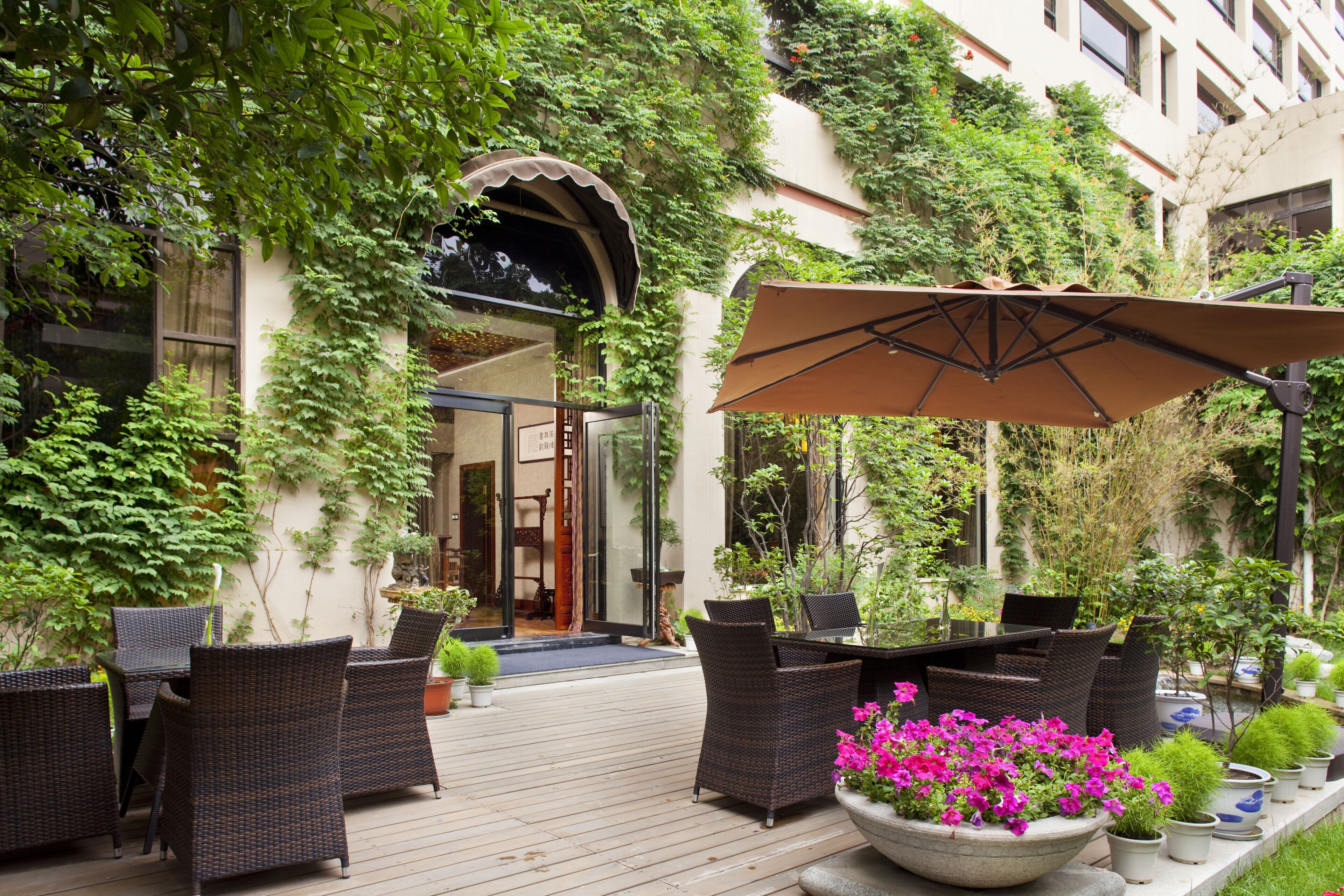 An outdoor seating area with wicker furniture, a large umbrella, and potted plants.