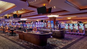 Zona de casino con múltiples máquinas de juego, un bar central y suelo cubierto de alfombra.