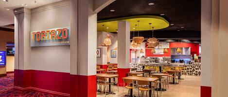 L’intérieur d’un restaurant présente une décoration aux couleurs rouge et blanche, avec de nombreuses tables et une cuisine ouverte.