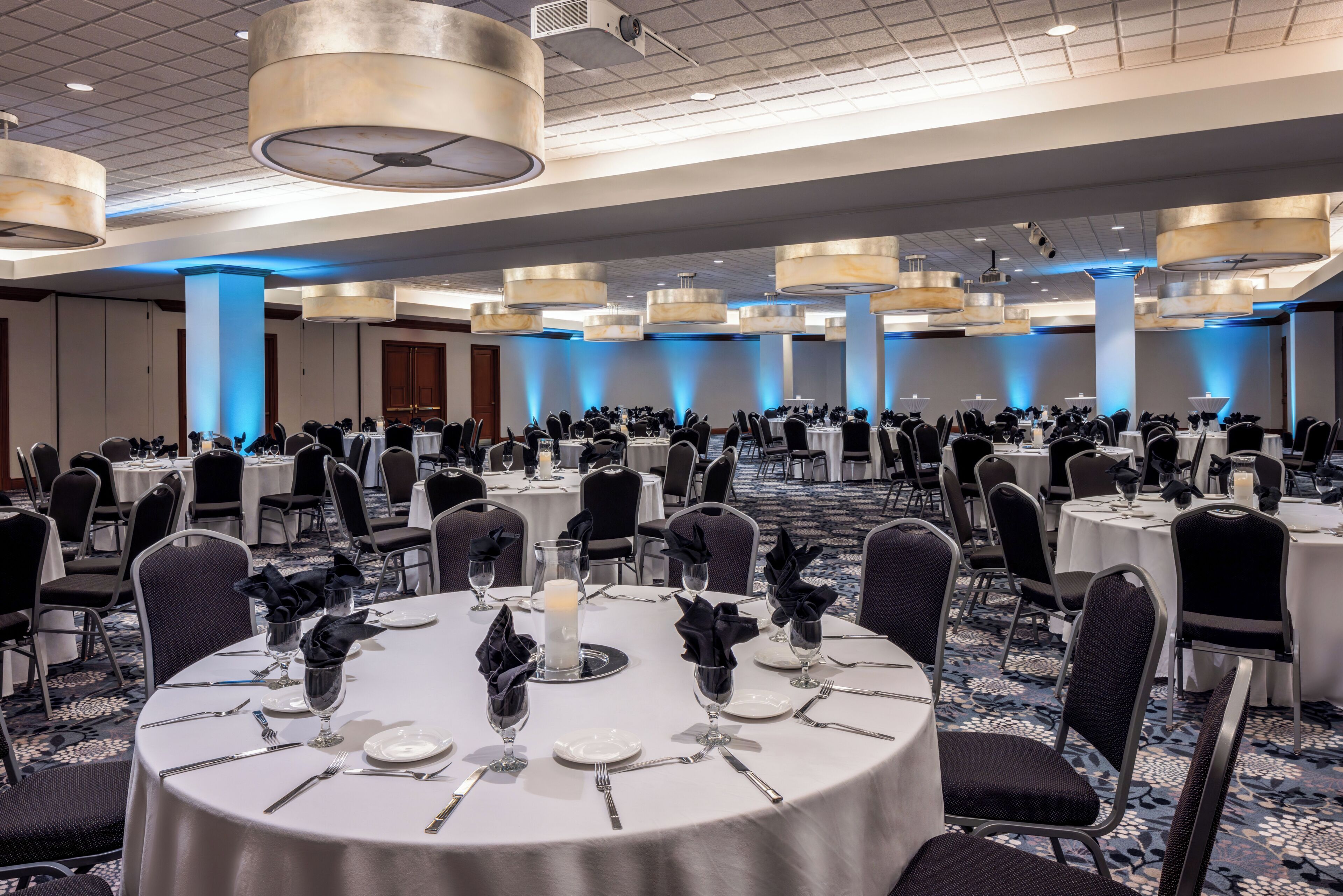 A banquet hall with round tables, chairs, and a ceiling with recessed lighting.