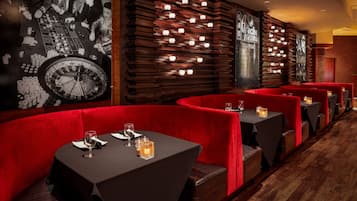 A row of red upholstered booths with tables, each with a candle and a wine glass.