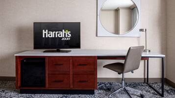 Habitación de hotel con escritorio, televisor mostrando 'Harrah's Joliet', espejo y una silla.