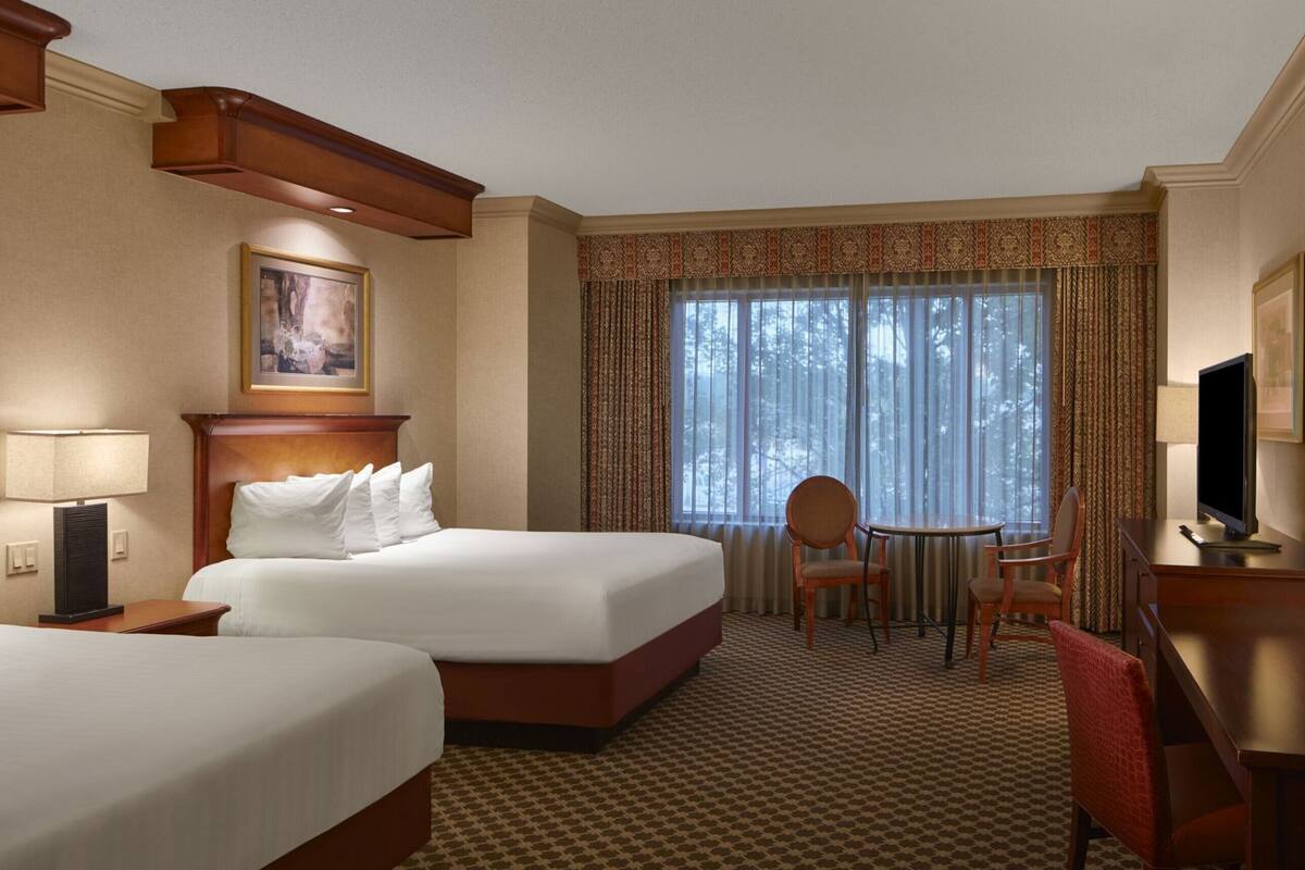 A hotel room with two beds, a desk, a chair, and a television.