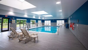 An indoor swimming pool with clear glass ceilings, blue walls, and wooden lounge chairs. - Hampton Inn Seaford (Seaford)