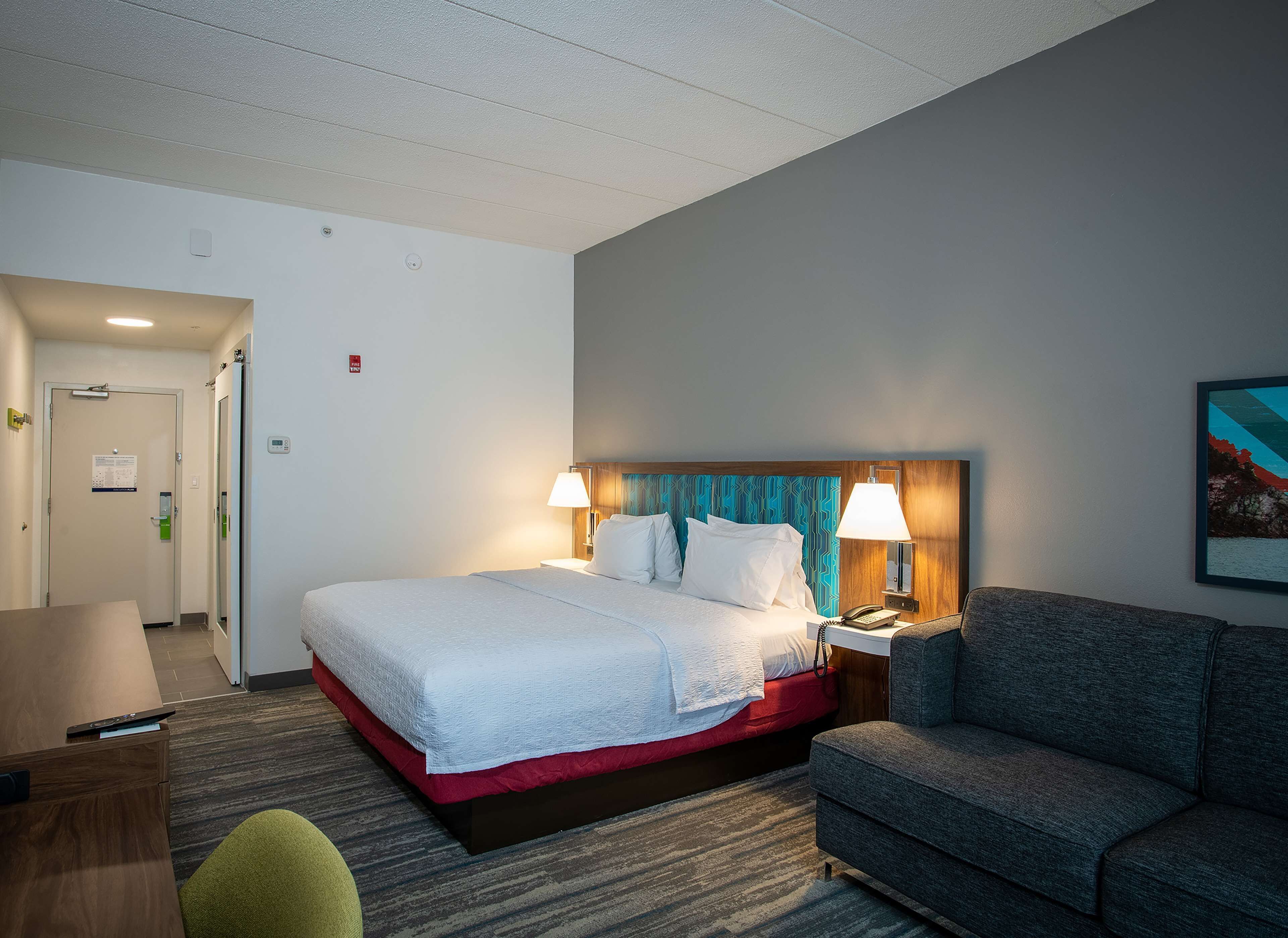 Ein Hotelzimmer mit Bett, Nachttischlampen, Schreibtisch, Stuhl und einem Bild an der Wand.
