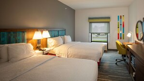 A hotel room with two beds, a desk with a chair, a window with a view, and a wall with colorful decor. - Hampton Inn Seaford (Seaford)
