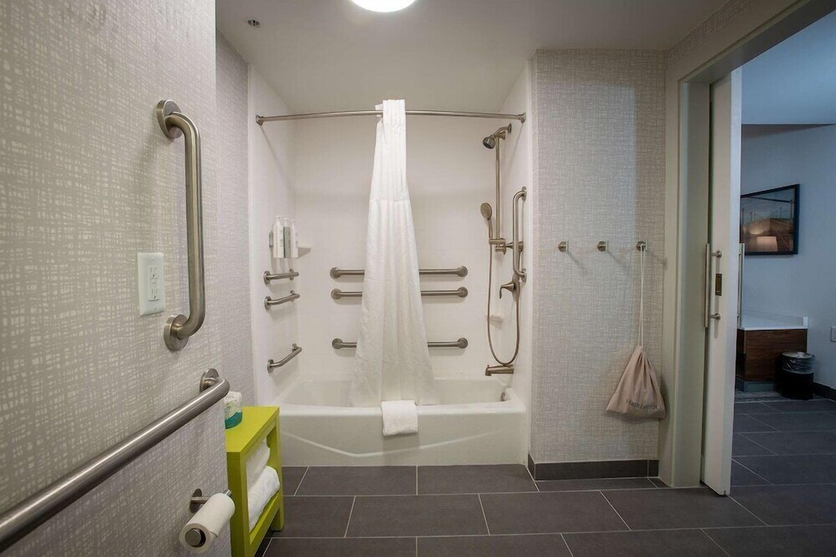 Un baño moderno con cabina de ducha, barras de apoyo, bañera y retrete con barra de apoyo.