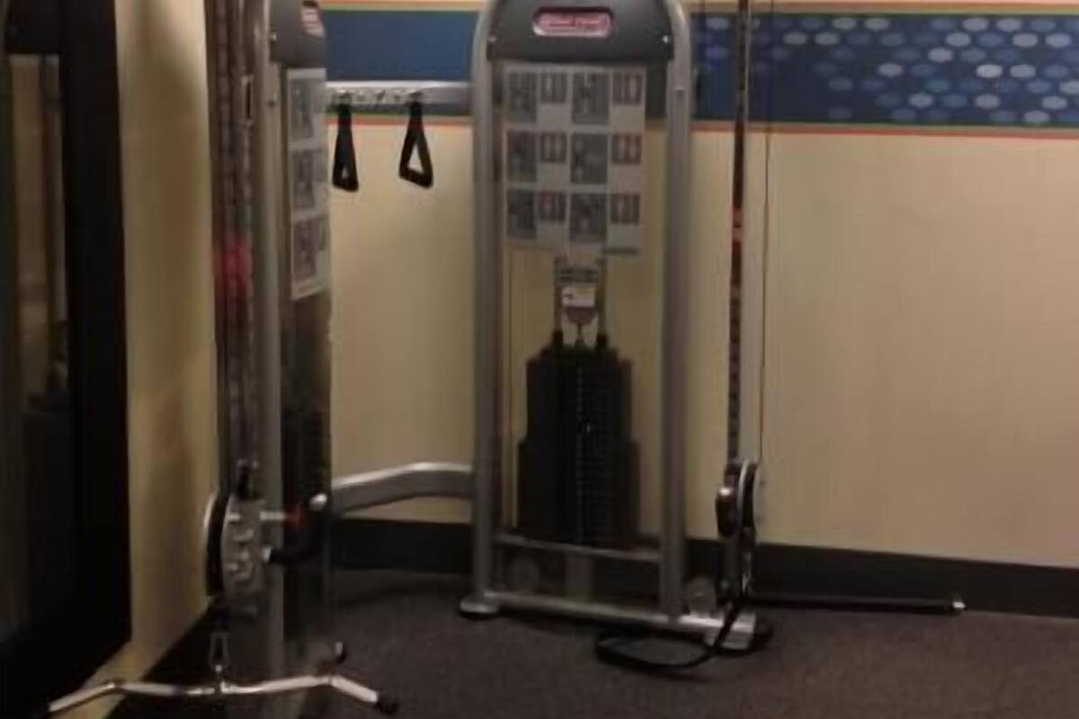 Uma academia com equipamentos de exercícios, um relógio na parede e uma porta à esquerda.