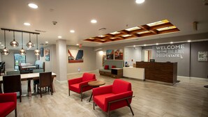 A modern reception area with a wooden reception desk, red seating, and a "Welcome to the Blue Hen State" sign. - Hampton Inn Seaford (Seaford)