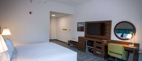 Una habitación de hotel con cama, escritorio, silla, televisor y lámpara.
