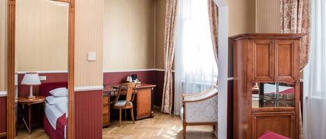 A hotel room with a bed, a desk, a chair, a wardrobe, and a mirror.