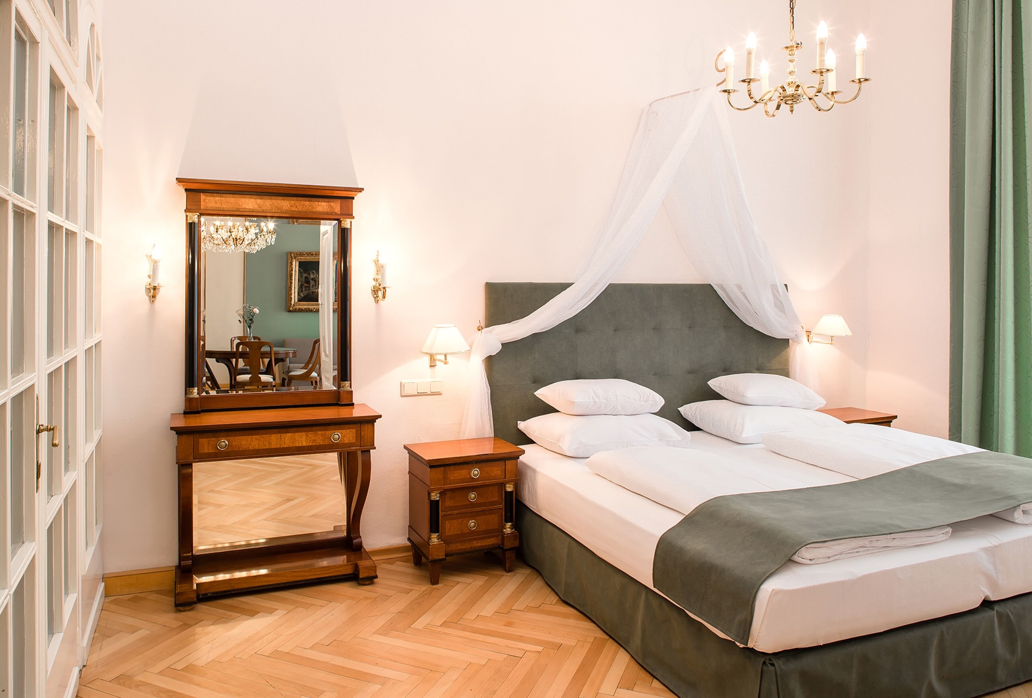 A bedroom with a bed, bedside tables, a mirror, and a chandelier.