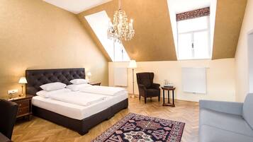 A bedroom with a large bed, a chandelier, a patterned rug, and a view of the sky through a skylight.