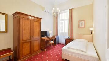 Ein Hotelzimmer mit Bett, Schreibtisch mit Stuhl, Kleiderschrank, Fernseher und einem Fenster mit Vorhängen.