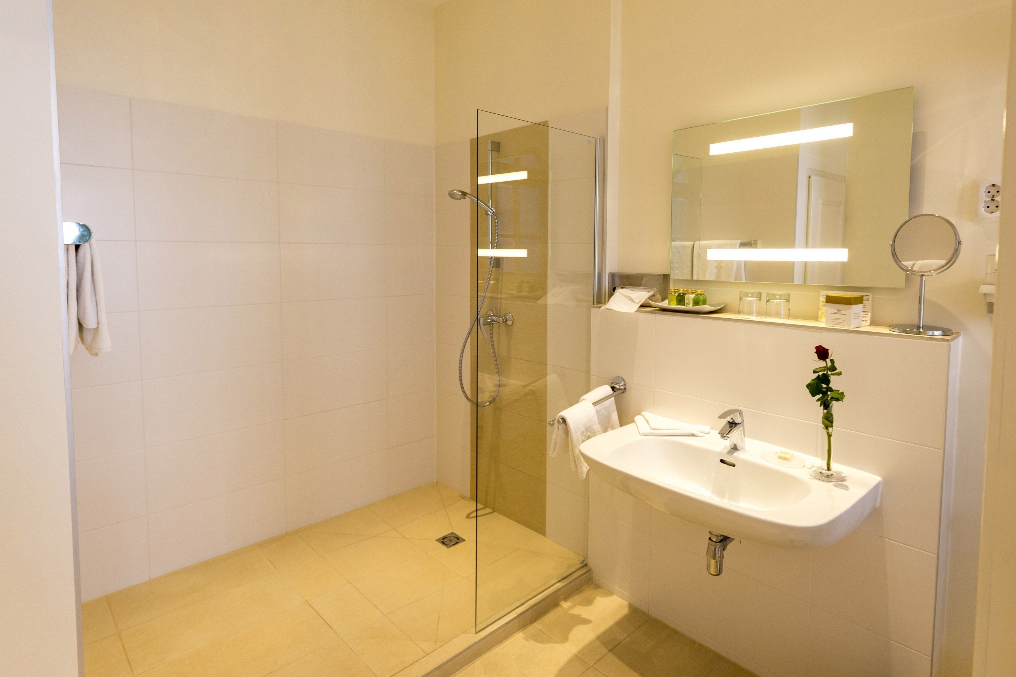 A modern bathroom with a glass-enclosed shower, a sink with a mirror, and a vase with a single rose.