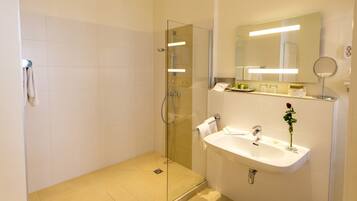 A modern bathroom with a glass-enclosed shower, a sink with a mirror, and a vase with a single rose.