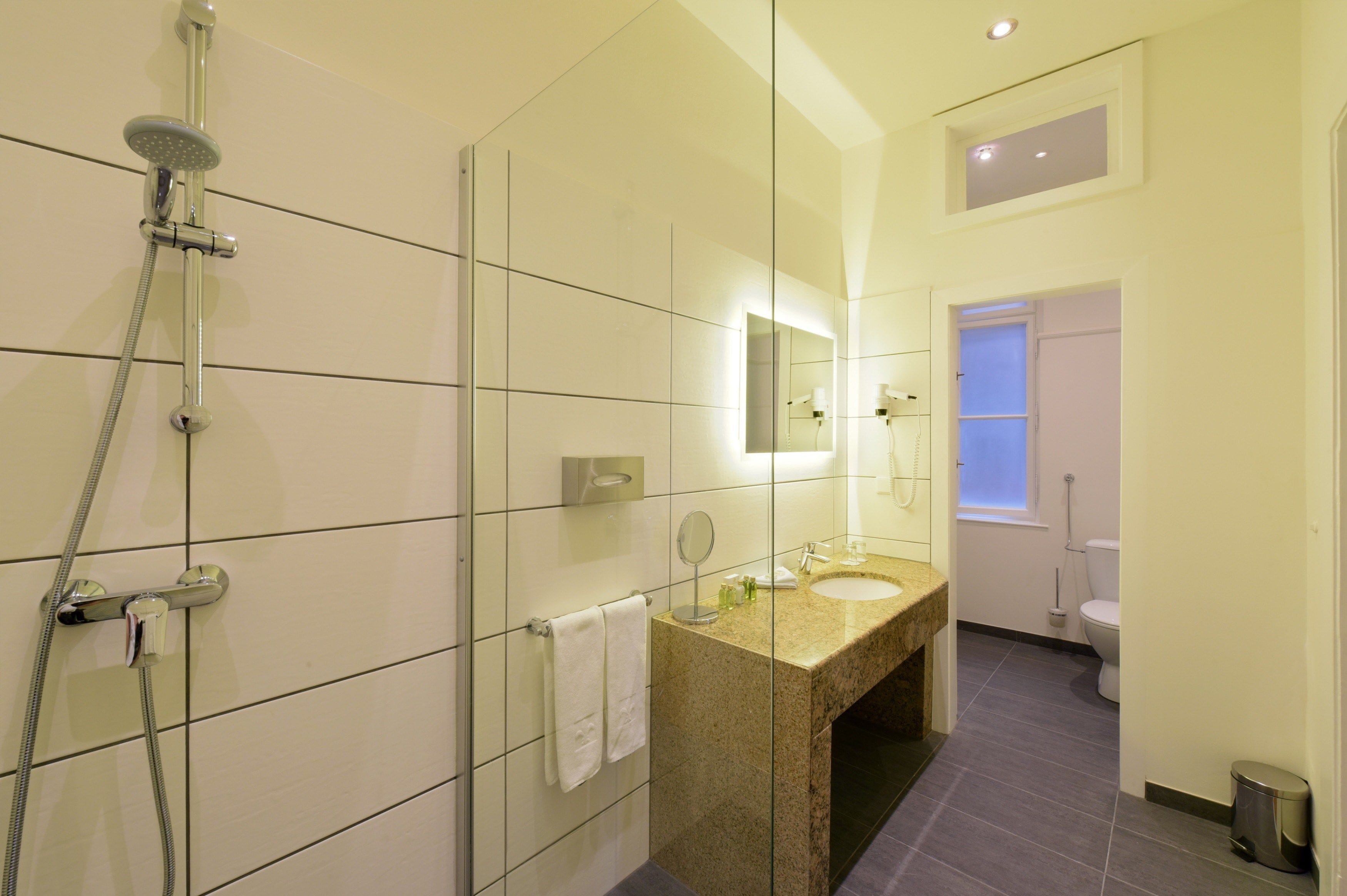 Un baño moderno con ducha envuelta en vidrio, lavamanos de granito y un espejo grande.