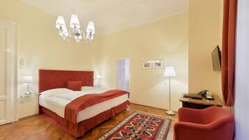 A bedroom with a bed, a red chair, a desk with a lamp, and a chandelier.