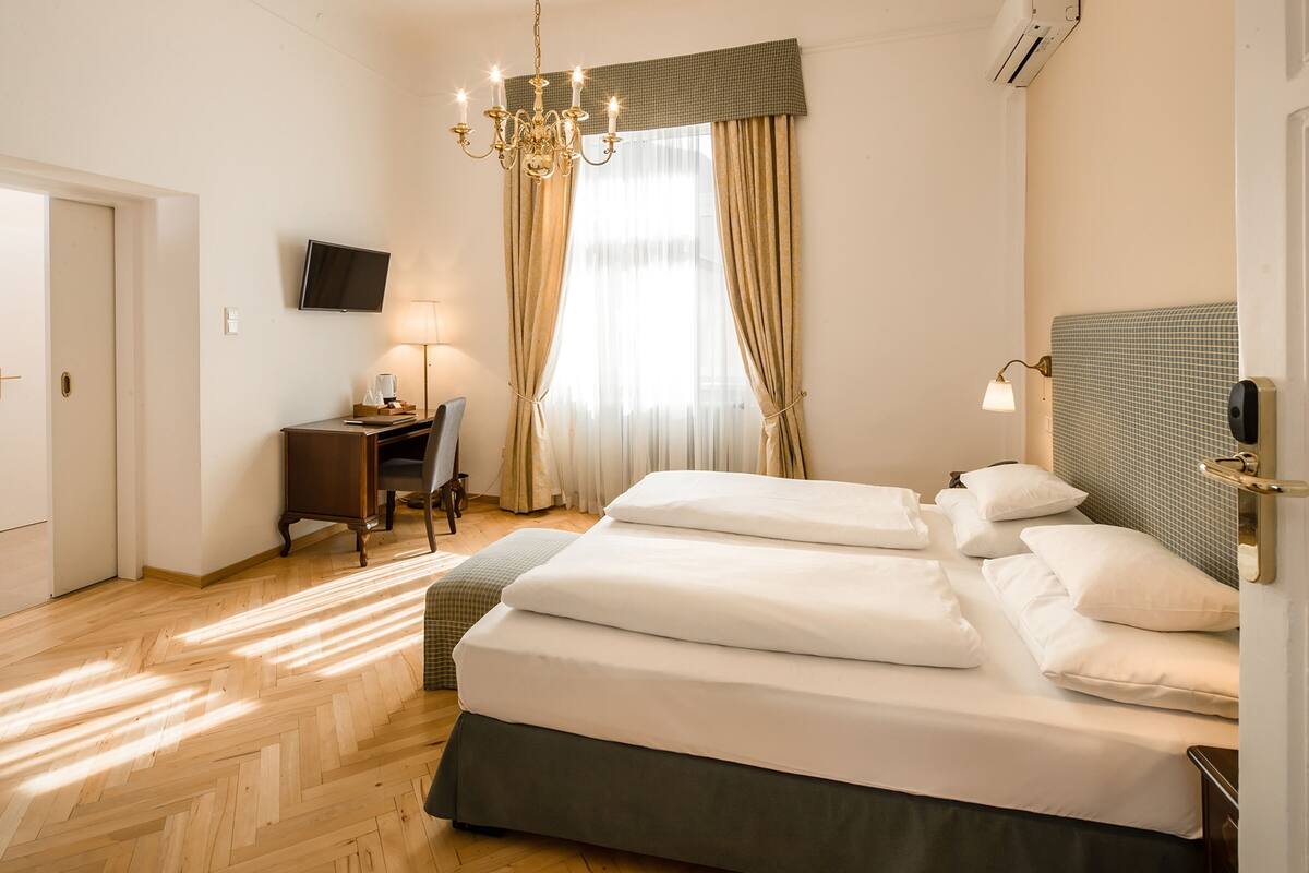 Une chambre d’hôtel avec un lit, un bureau, une chaise, une télévision et un lustre.