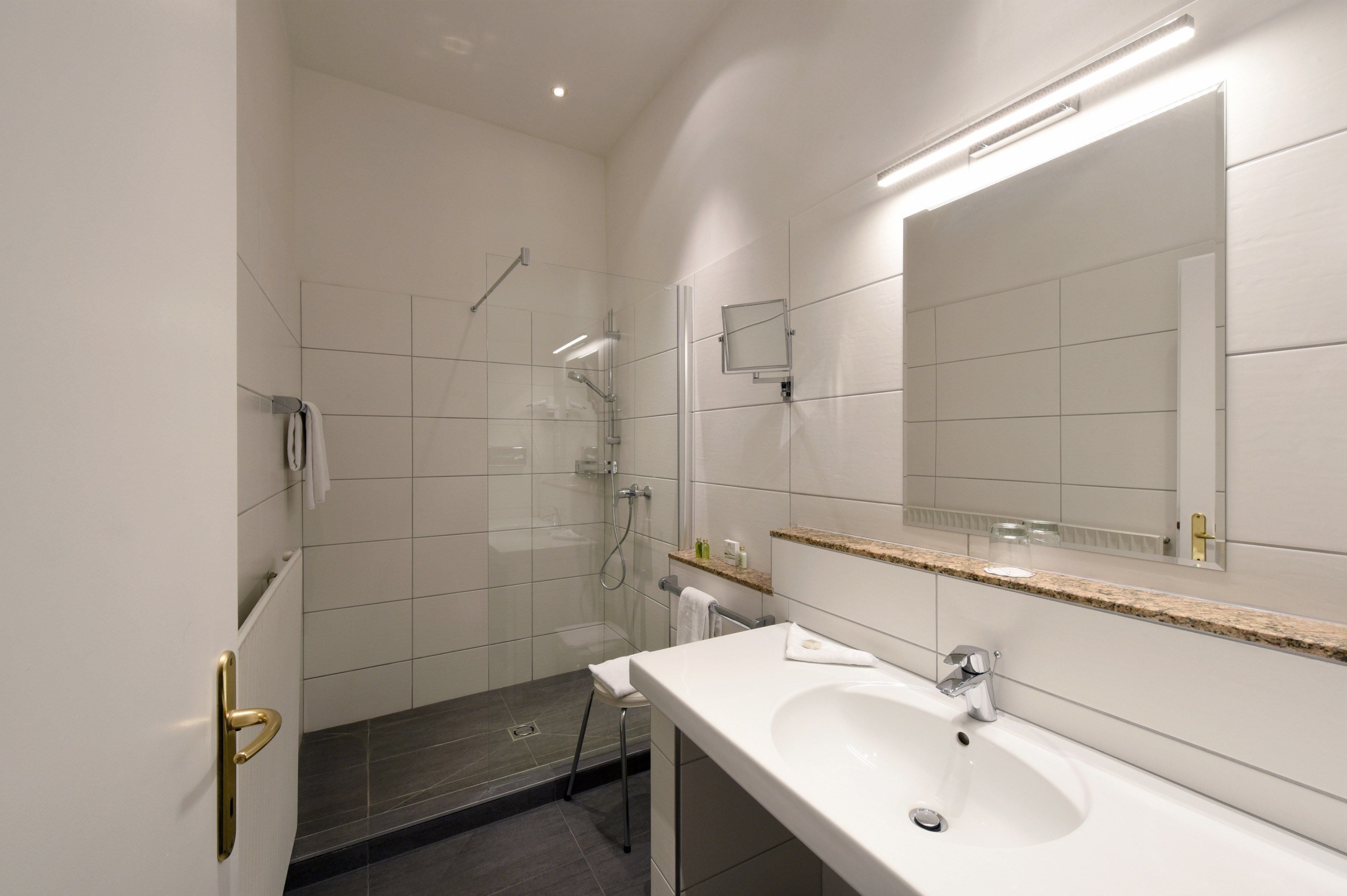 A modern bathroom with a glass-enclosed shower, a white sink, and a large mirror.