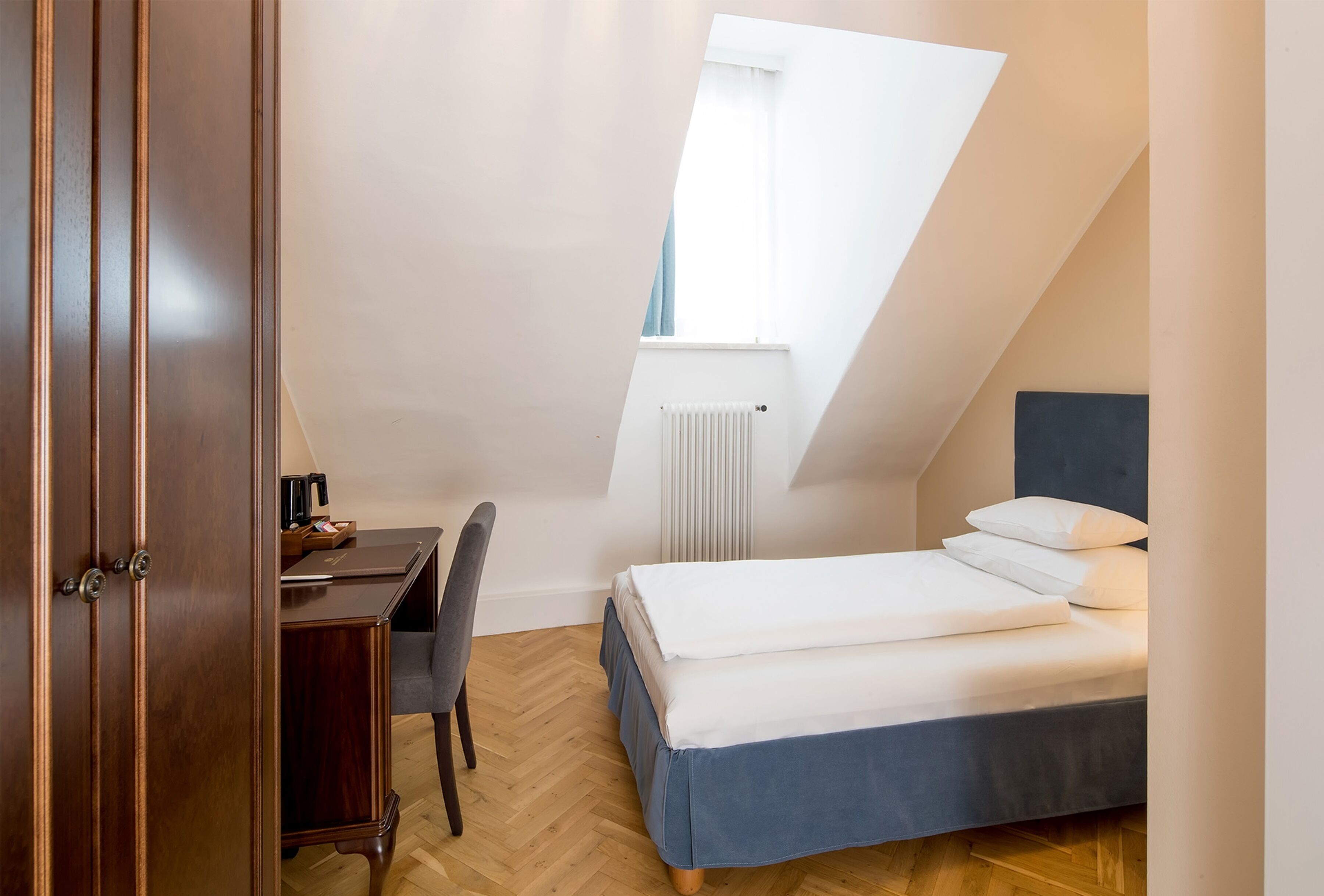 A bedroom with a bed, a desk, and a chair. There is a window with a view of the sky.