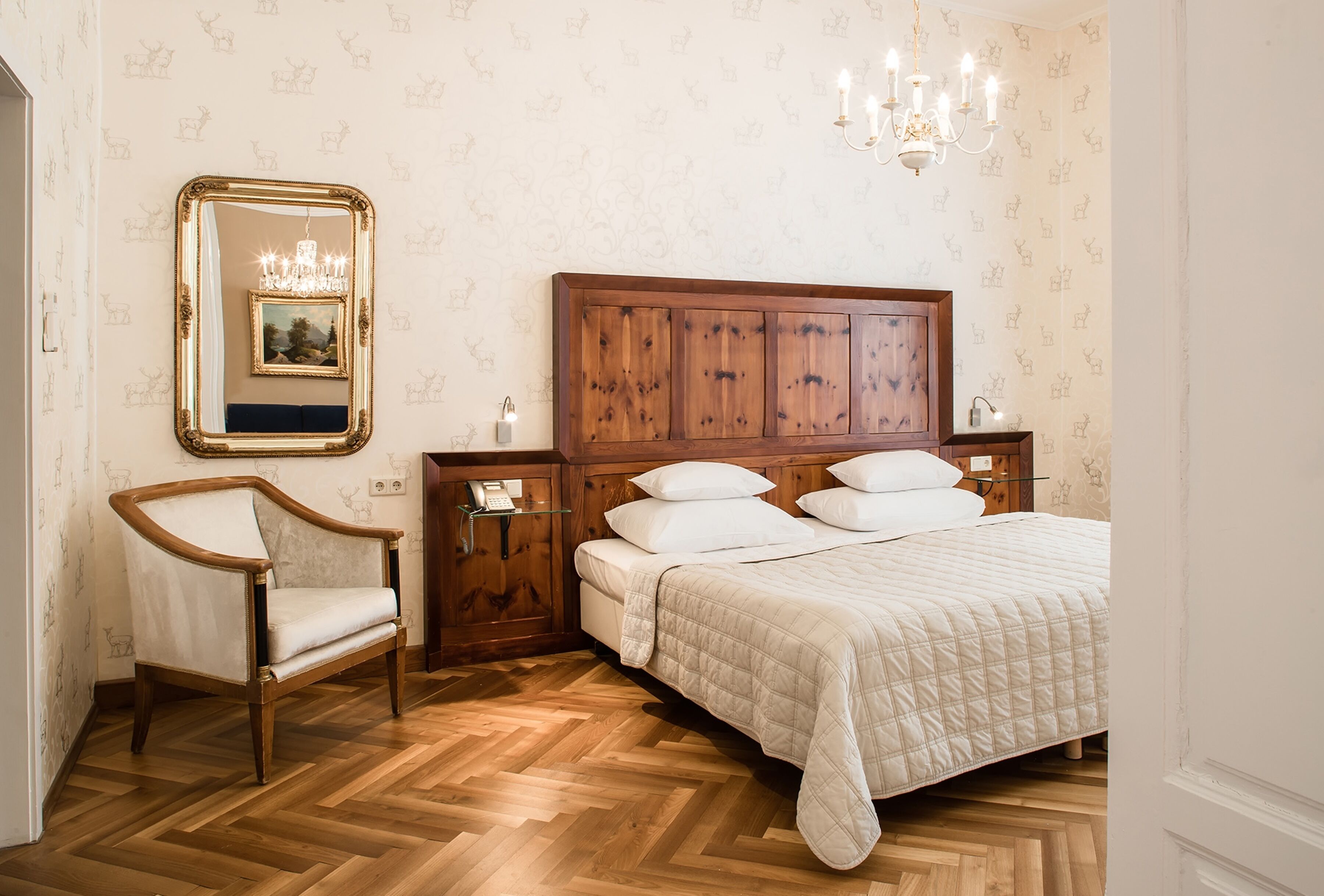 A bedroom with a wooden headboard, a large mirror, a chandelier, and a wooden floor.