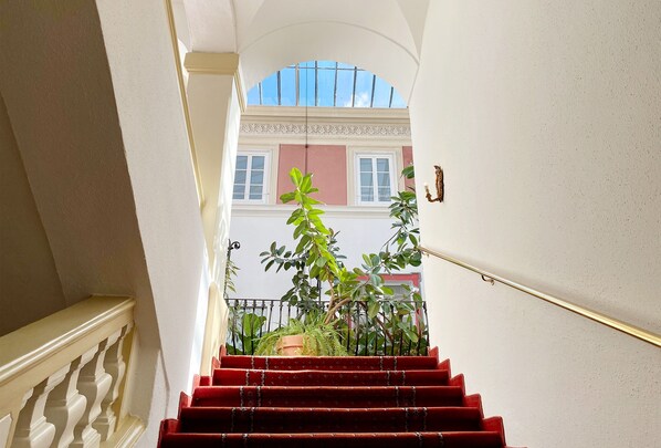 Una escalera con peldaños rojos lleva a un balcón que ofrece vistas de un edificio de paredes rosadas y blancas.