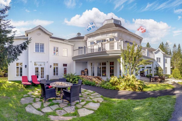 A large, white, two-story house with a balcony, stone pathway, and outdoor seating area. - Hilton Grand Vacations Club Tremblant Canada (Mont-Tremblant)