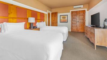 A hotel room with two beds, a wooden headboard, a television, a desk with a lamp, and a wardrobe.
