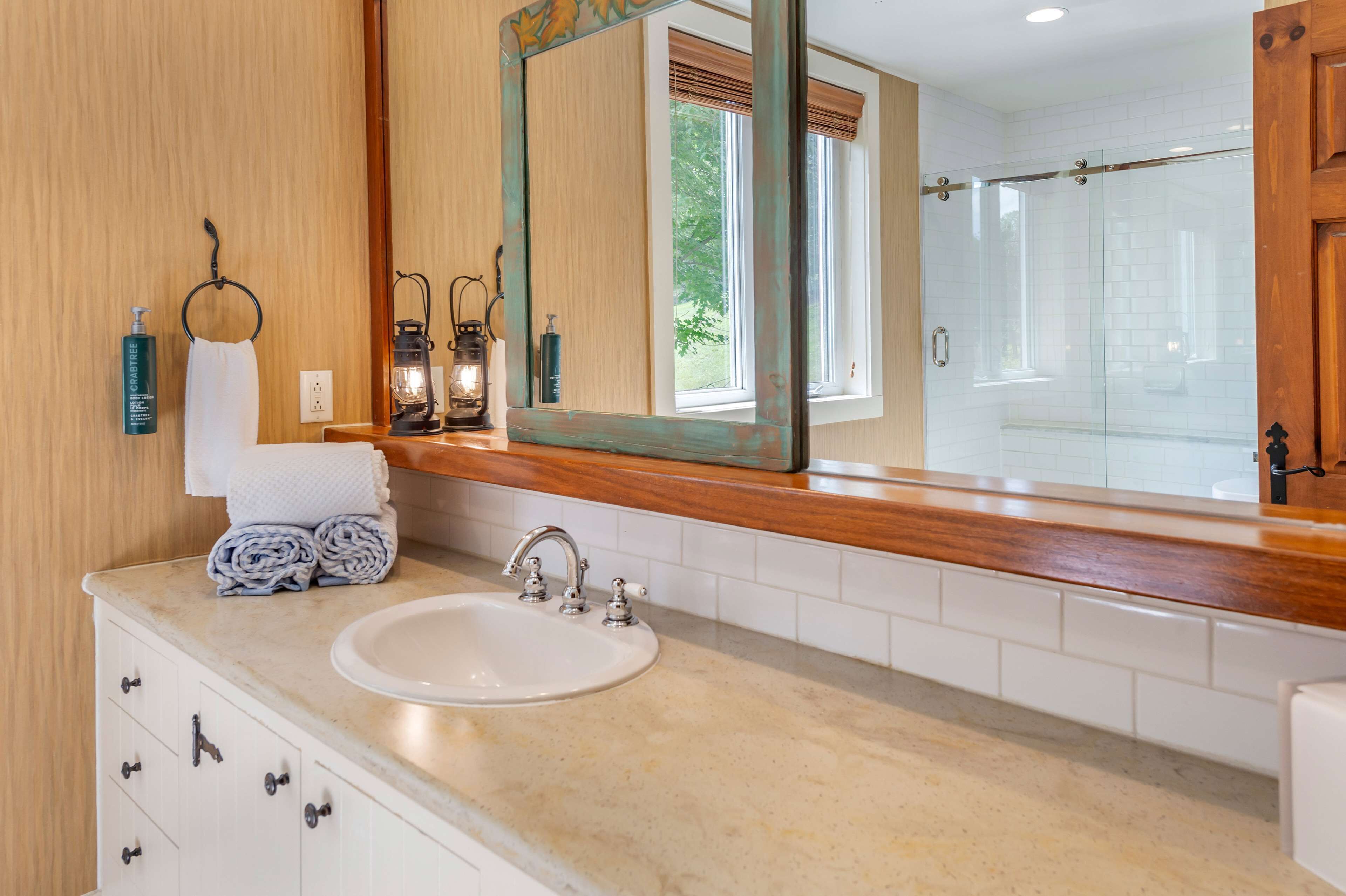 A bathroom with a large mirror, a sink, and a shower area.