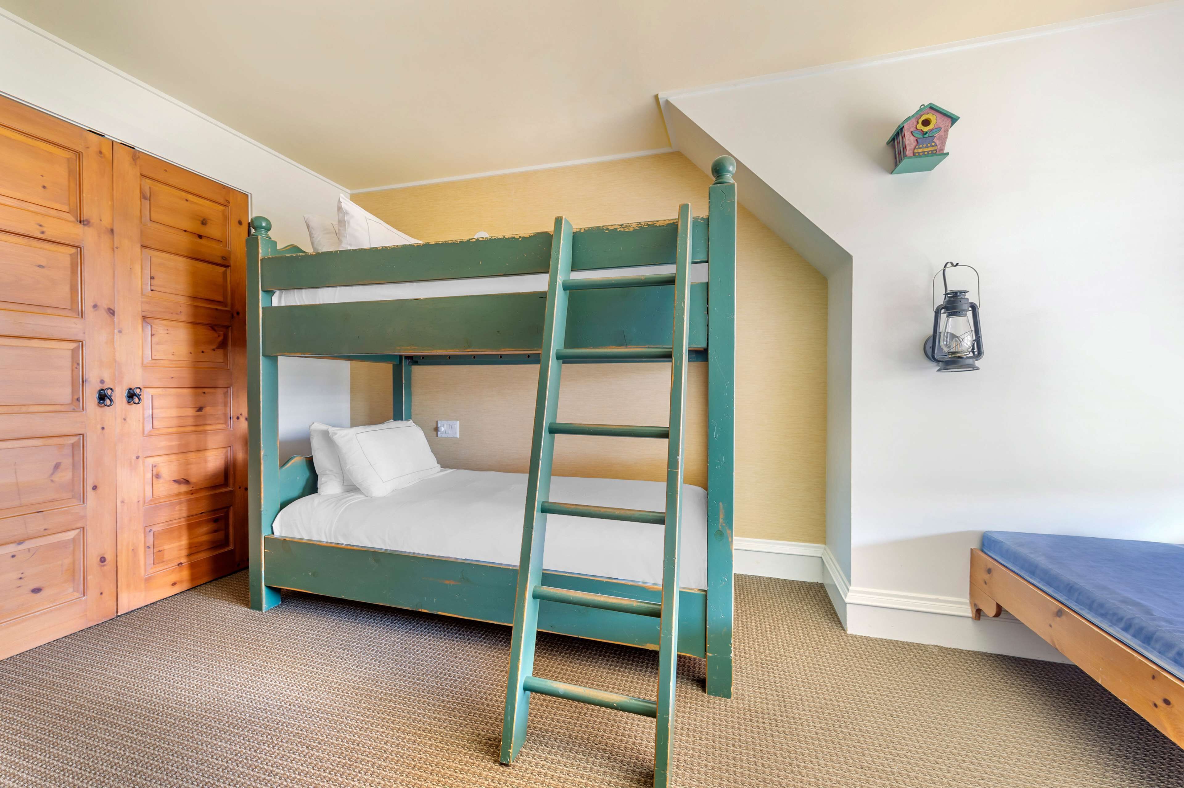 A bunk bed with a ladder, a wooden wardrobe, and a small birdhouse on the wall.