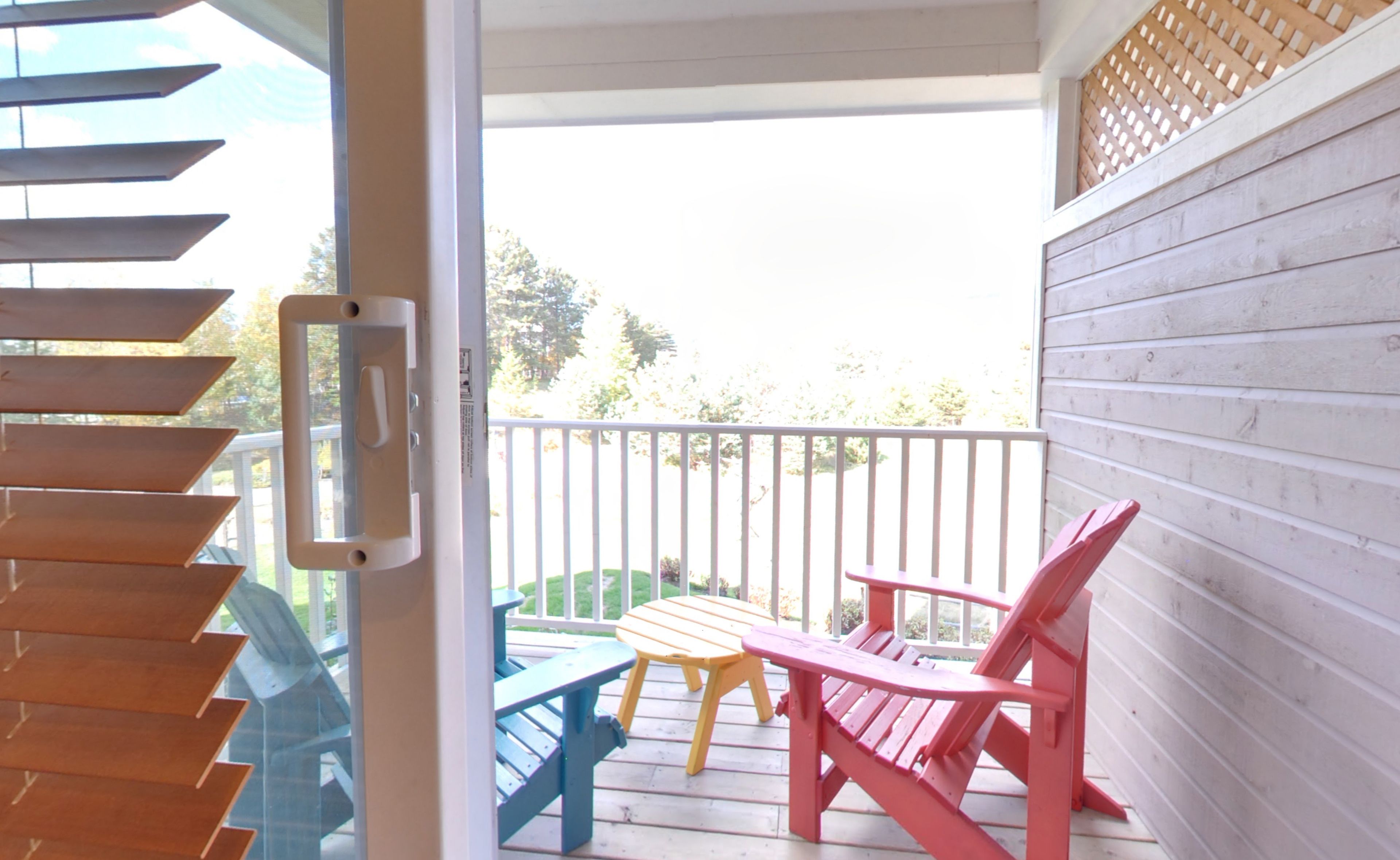 Un espacio al aire libre techado con una terraza de madera, una silla roja y una silla azul, junto a una pequeña mesa.