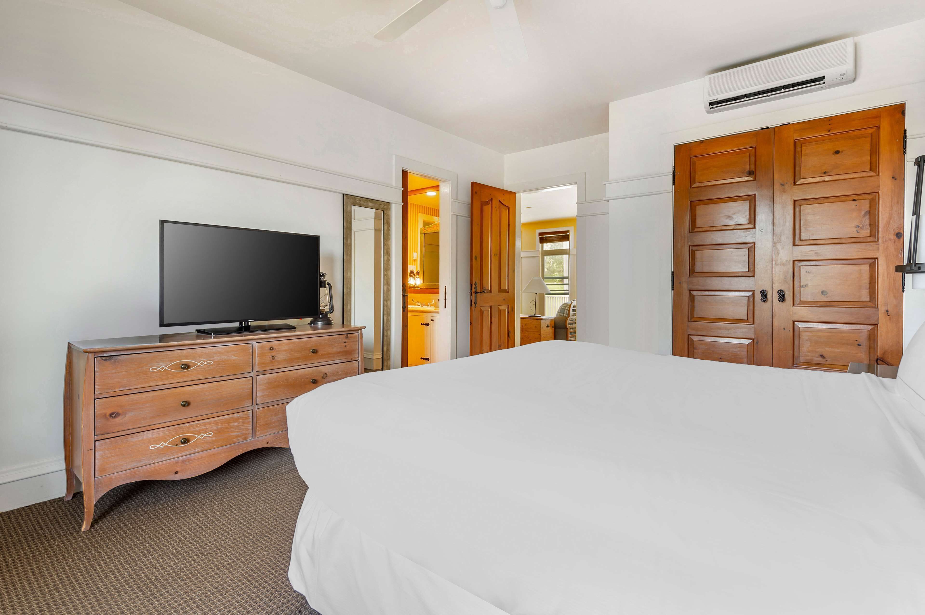 Une chambre d’hôtel avec un grand lit, une commode en bois, une télévision et un miroir.