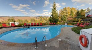 A swimming pool with red lounge chairs, a lifebuoy, and a view of mountains. - Hilton Grand Vacations Club Tremblant Canada (Mont-Tremblant)